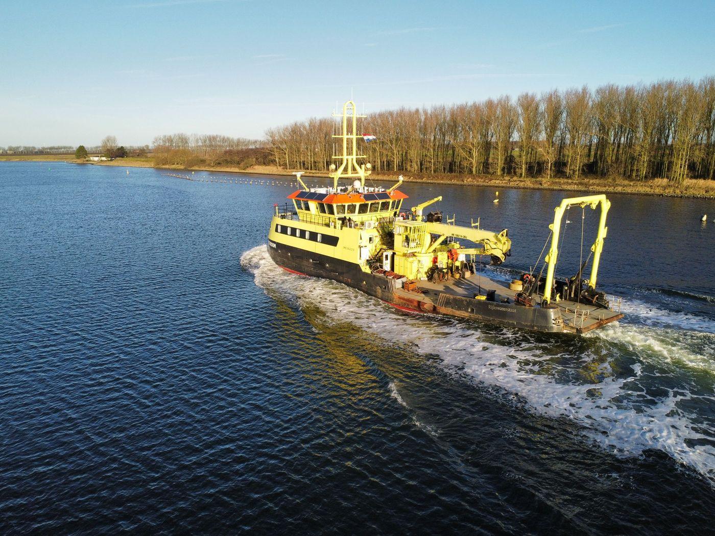 A survey vessel under way on calm water beneath a clear sky